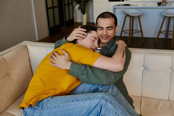 A young gay couple cuddles on a white couch in their modern apartment. — Stock Photo