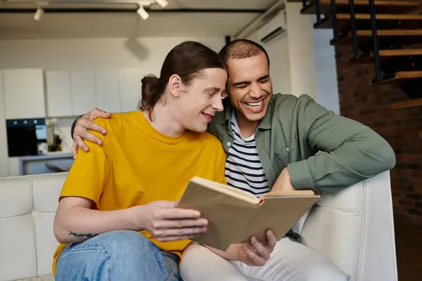 Um jovem casal gay compartilha uma risada ao ler um livro juntos em um apartamento moderno. — Fotografia de Stock