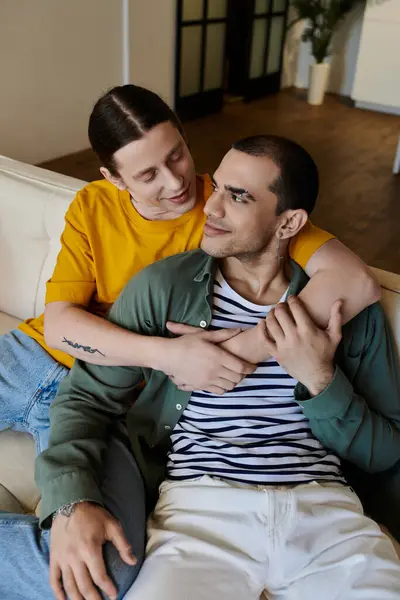 A young gay couple cuddles on a couch in their modern apartment, enjoying quality time together. — Stock Photo