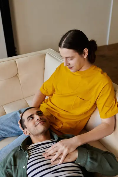 Ein junges schwules Paar entspannt sich auf einem Sofa in seiner modernen Wohnung und genießt einen Moment der Intimität. — Stockfoto