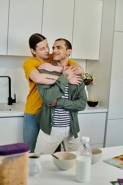 A young gay couple enjoys a morning embrace in a bright, modern kitchen. — Stock Photo