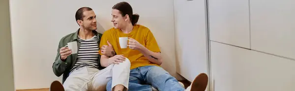 Un jeune couple gay partage un moment tendre dans leur appartement moderne, dégustant un verre ensemble. — Photo de stock