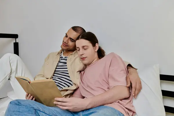 Um jovem casal gay relaxa em uma cama em um apartamento moderno, um lendo um livro enquanto o outro descansa a cabeça em seu ombro. — Fotografia de Stock