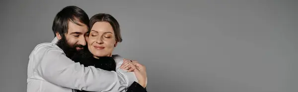 Un homme barbu embrasse une femme, tous deux vêtus de vêtements sophistiqués, dans un moment tendre sur fond gris. — Photo de stock