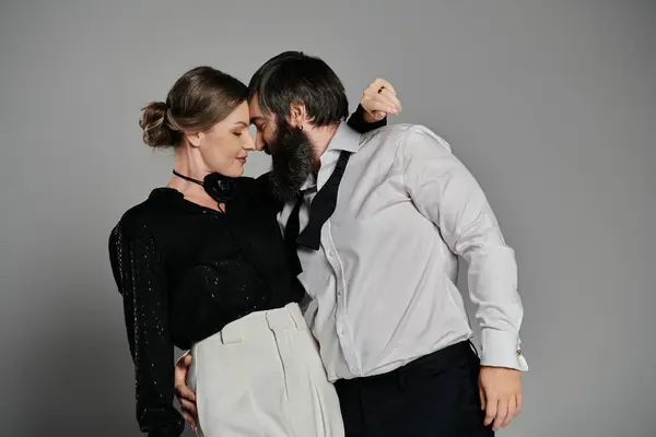 Una pareja amorosa, vestida con trajes sofisticados, posan juntos sobre un fondo gris. - foto de stock