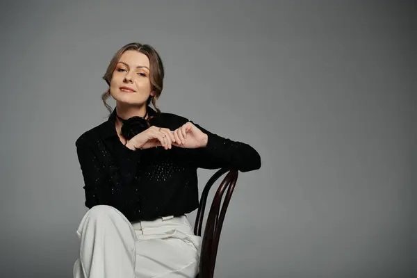 A woman in a black blouse and white pants sits on a chair, looking confidently at the camera. — Stock Photo