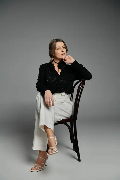 A woman in a black blouse and white pants sits on a chair, looking off to the side. — Stock Photo