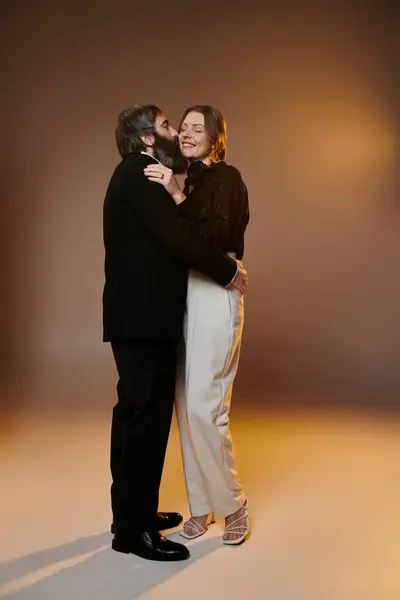 Ein Paar in eleganter Kleidung posiert zusammen, der Mann küsst die Wange der Frau, erleuchtet von warmem, goldenem Licht. — Stockfoto