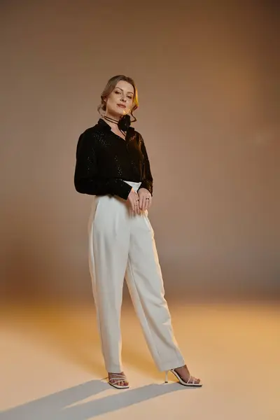 A woman in a black blouse and white pants poses in a studio setting. — Stock Photo