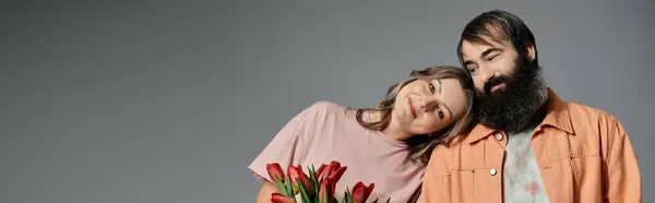 A man and a woman in sophisticated attire pose together, with the woman holding a bouquet of red tulips. — Stock Photo