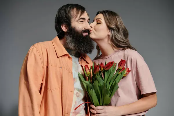 A loving couple in sophisticated attire shares a tender moment, the woman holding a bouquet of tulips. — Stock Photo
