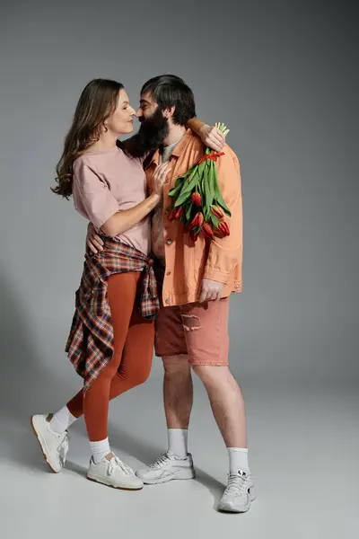 A loving couple poses together, the woman holding a bouquet of red tulips and looking lovingly at the man. — Stock Photo