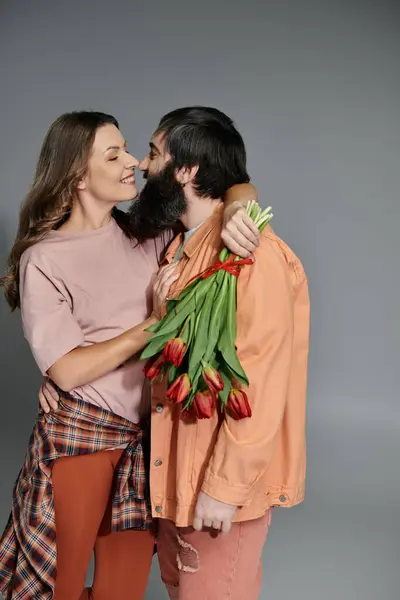 A loving couple poses for a portrait, with the woman embracing the man who holds a bouquet of red tulips. — Stock Photo