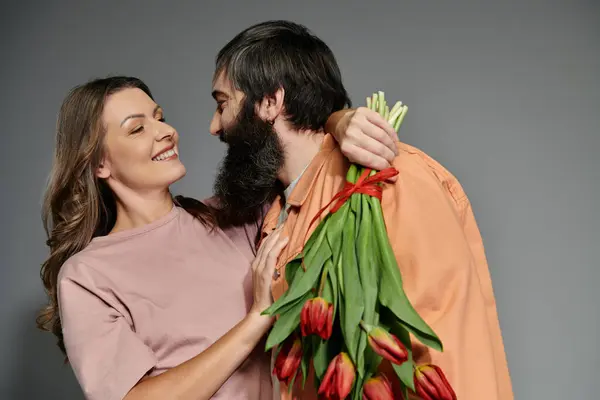A couple in sophisticated attire embraces, the woman smiling as she holds a bouquet of red tulips. — Stock Photo