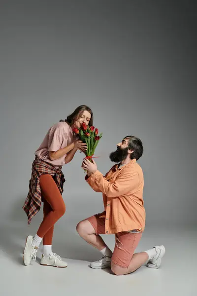 A man kneels before a woman, presenting her with a bouquet of red tulips, in a studio setting. — Stock Photo