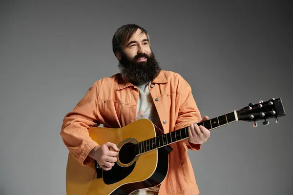 A man with a beard plays an acoustic guitar in a studio with a grey background. — Stock Photo
