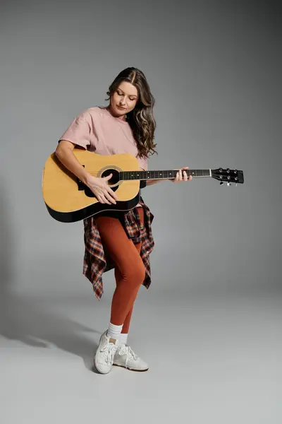 A young woman in stylish attire strums an acoustic guitar with passion. — Stock Photo