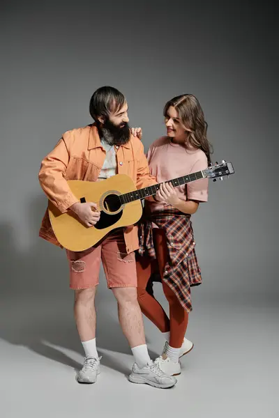 Um casal posa juntos em um estúdio, o homem tocando uma guitarra, enquanto a mulher se inclina e sorri. — Fotografia de Stock