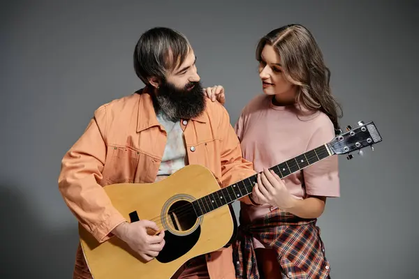 A loving couple poses together in a studio setting, the man playing a guitar and the woman looking on lovingly. — Stock Photo