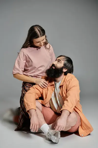 Un couple est assis dans un studio, la femme en chemise rose et pantalon à carreaux, l'homme en veste orange et short, se regardant avec amour. — Photo de stock