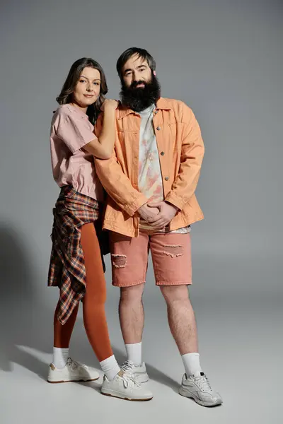 A loving couple poses together, the woman in a pink shirt and brown leggings, the man in a peach jacket and shorts. — Stock Photo