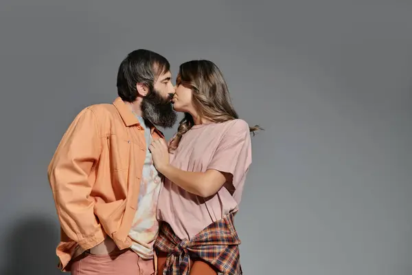 A couple in stylish attire share a passionate kiss against a plain gray backdrop. — Stock Photo