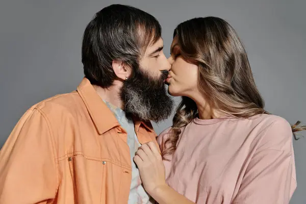 Um casal em traje sofisticado amorosamente beijo contra um pano de fundo cinza. — Fotografia de Stock