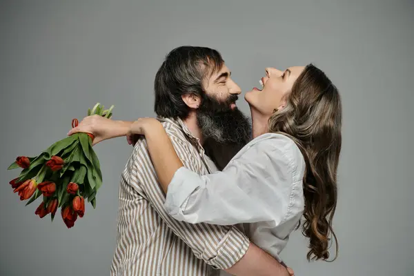 A man and woman in stylish attire embrace with a bouquet of tulips. — Stock Photo