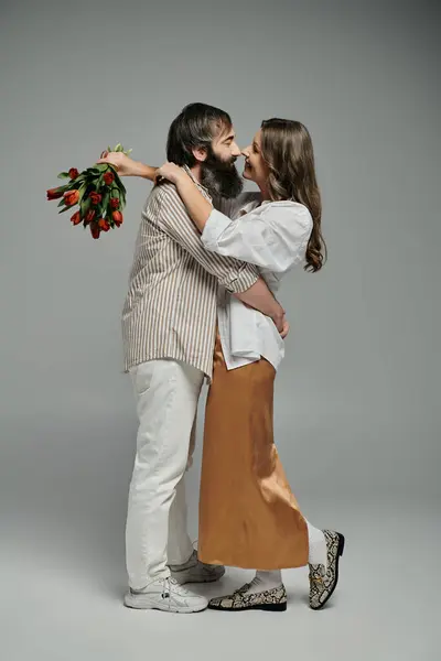 A loving couple in sophisticated attire embraces with a bouquet of tulips. — Stock Photo