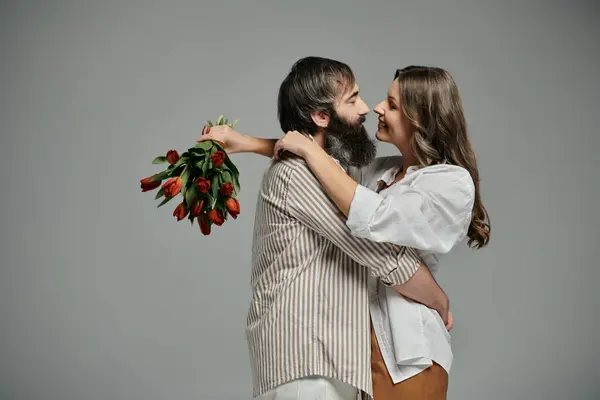 Un couple en tenue sophistiquée embrasse, la femme tenant un bouquet de tulipes rouges. — Photo de stock