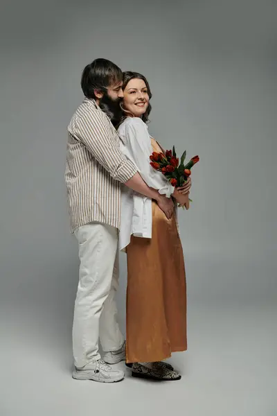A couple dressed in stylish attire embraces, the woman holding a bouquet of red flowers. — Stock Photo
