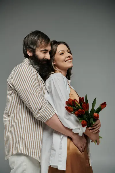 Um casal em trajes sofisticados abraça, a mulher segurando um buquê de tulipas vermelhas. — Fotografia de Stock