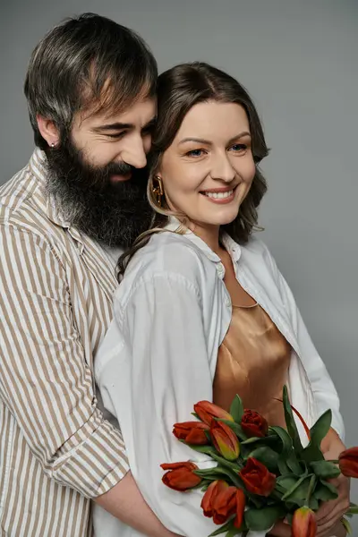 A couple in elegant attire, the man holding the woman close as she smiles and holds a bouquet of tulips. — Stock Photo
