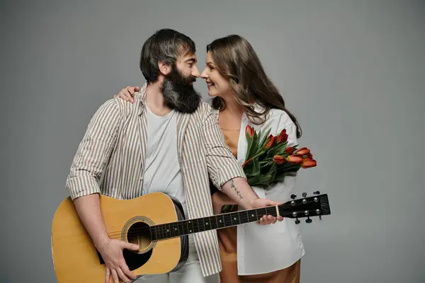 A couple dressed in sophisticated attire poses together, the man holding an acoustic guitar and the woman holding a bouquet of red tulips. — Stock Photo
