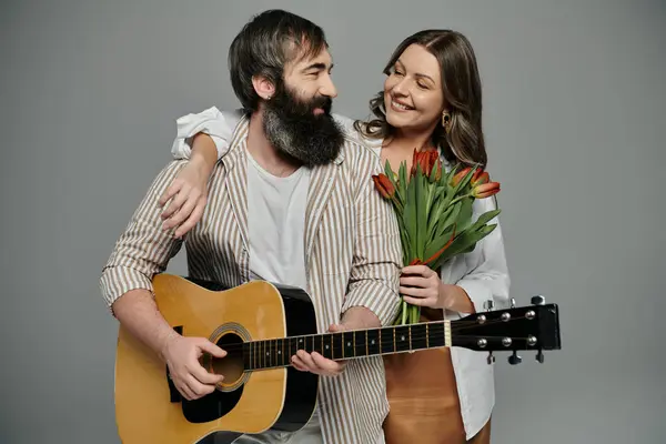 A couple poses together, the man playing a guitar and the woman holding a bouquet of tulips. — Stock Photo