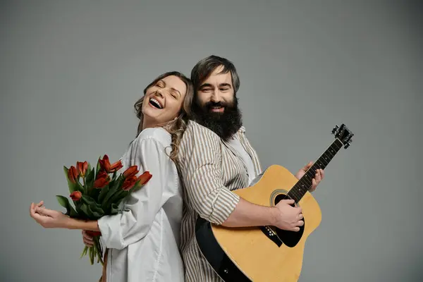 A man and woman in elegant attire pose together, the woman holding a bouquet of red tulips, while the man plays an acoustic guitar. — Stock Photo
