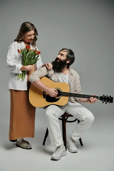 A couple in sophisticated attire poses for a photo, the man playing a guitar while the woman holds a bouquet of tulips. — Stock Photo