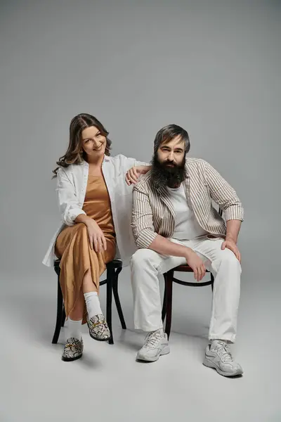 Un couple amoureux vêtu d'une tenue sophistiquée pose ensemble tout en étant assis sur des chaises dans un studio. — Photo de stock