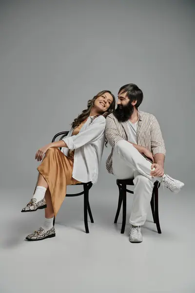 A man and woman, dressed in stylish attire, sit on chairs and look lovingly at each other. — Stock Photo