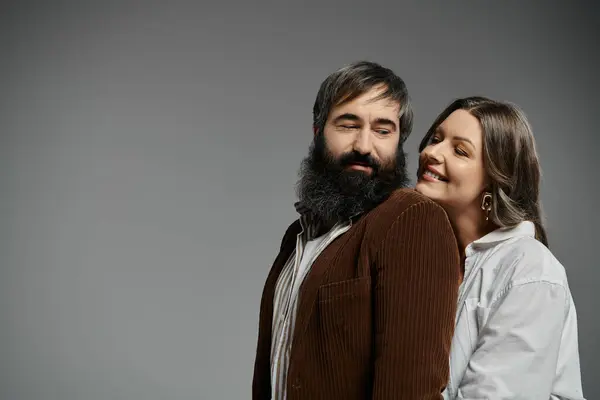 Una coppia amorevole posa insieme, l'uomo in giacca di velluto marrone e la donna in camicia bianca, su uno sfondo grigio chiaro. — Foto stock
