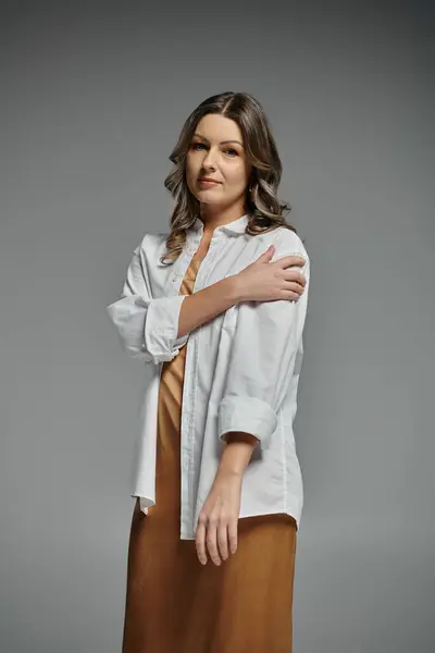 A woman in a white shirt and brown skirt stands against a gray backdrop, exuding confidence. — Stock Photo