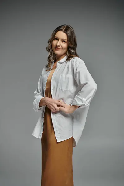 A woman in a white shirt and brown skirt poses against a gray backdrop. — Stock Photo
