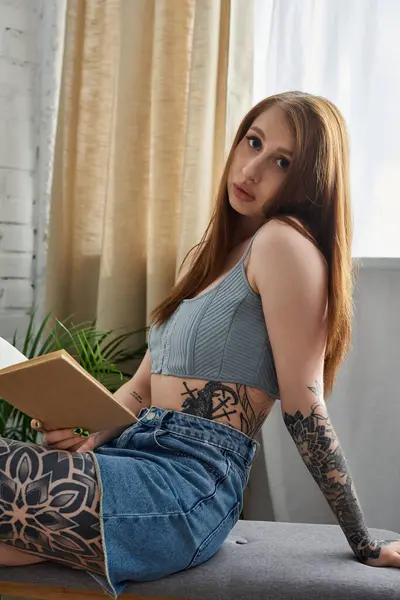 A young woman with tattoos sits comfortably in a modern apartment, enjoying a relaxing weekend at home. — Stock Photo