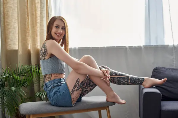 A young woman with tattoos relaxes on a bench in her modern apartment on a cozy weekend. — Stock Photo