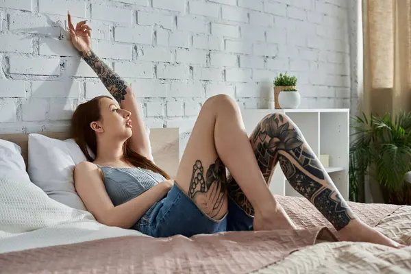 A young woman with tattoos relaxes on her bed, enjoying a cozy weekend at home. — Stock Photo
