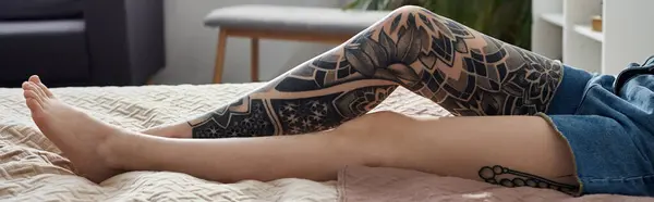 A tattooed womans leg rests on a bed in a modern apartment. — Stock Photo