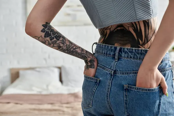 A young woman with tattoos on her arm and back stands in her modern apartment, enjoying a cozy weekend. — Stock Photo