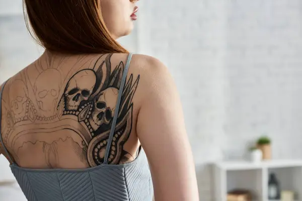 Una giovane donna con un grande tatuaggio sulla schiena si rilassa nel suo appartamento moderno. — Foto stock