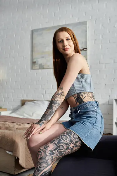 A young woman with tattoos sits on a couch in her modern apartment, enjoying a cozy weekend at home. — Stock Photo