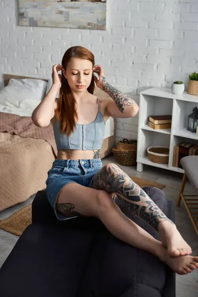 A young woman with tattoos relaxes on a couch in a modern apartment. — Stock Photo
